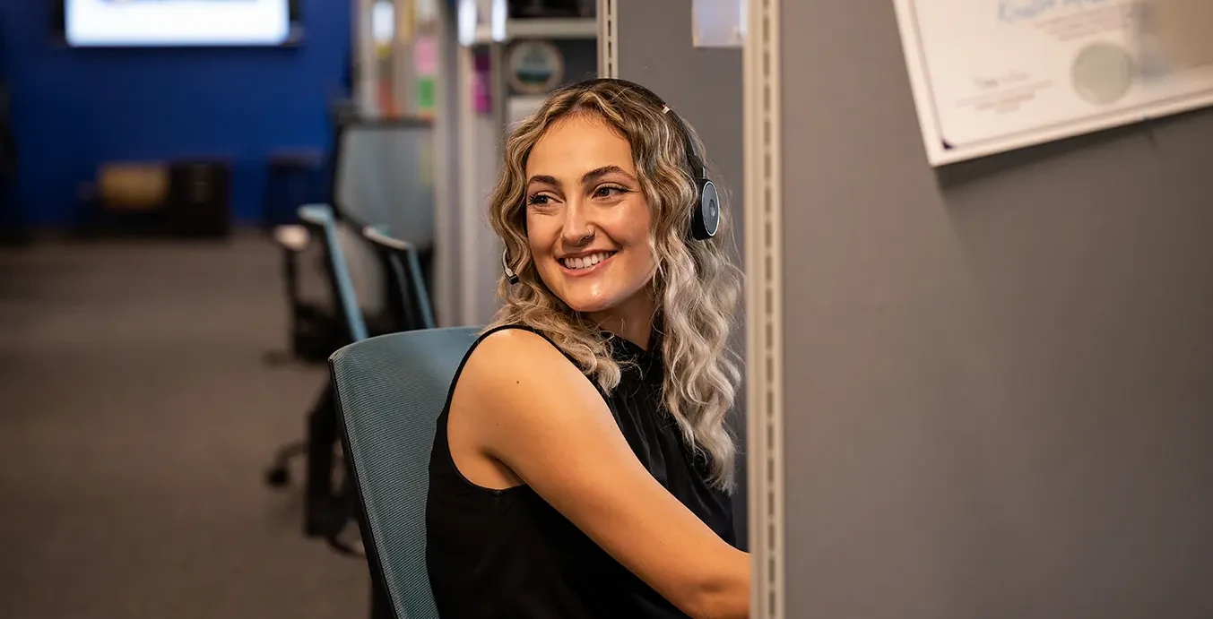 A Lady Wearing A Headset Sat At A Desk