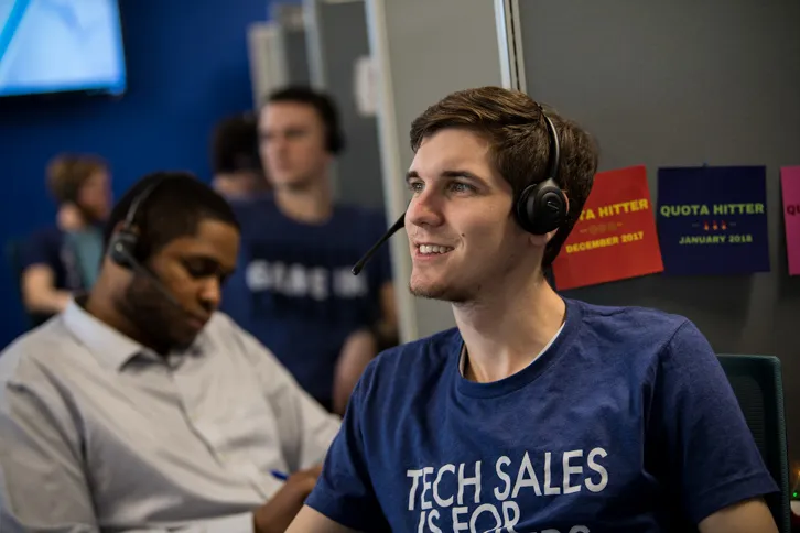 Two Men With Headsets In A Cubicle With Post It Notes On